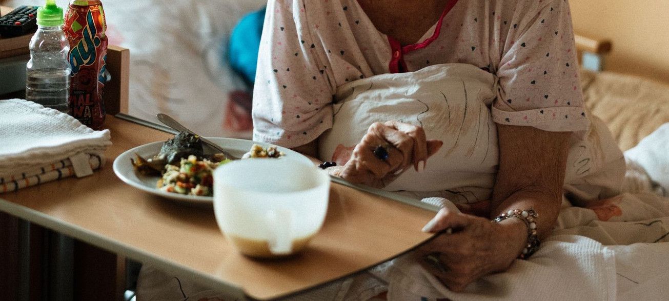 Elderly woman enjoying a meal in a cozy retirement home setting.